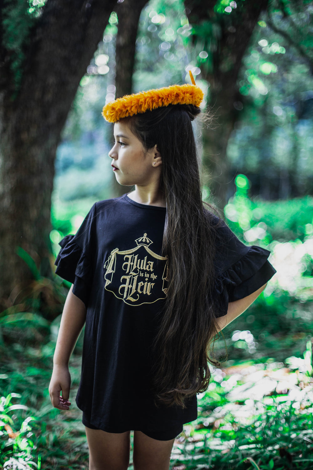 Our flirty, ruffled Līhau Blouse will make your little sweetie feel like the Queen she is! This top features our gold, metallic "Hula is in the Heir" code of arms design embroidered on the chest and made in a soft, viscose spandex.  