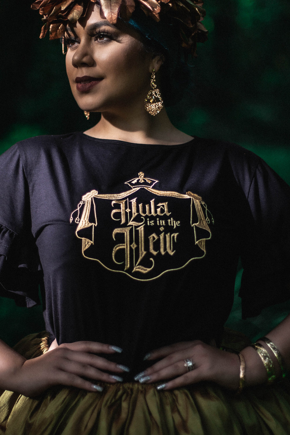 Our flirty, ruffled Līhau Blouse will make you feel like the Queen you are! This top features our gold, metallic "Hula is in the Heir" code of arms design embroidered on the chest and made in a soft, viscose spandex.  
